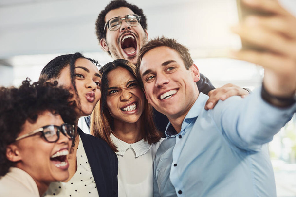 Teamwork, playful and selfie while a group of cheerful businesspeople making funny faces together for a social media post. Faces of a happy and fun team standing together in a creative office. - 写真・画像
