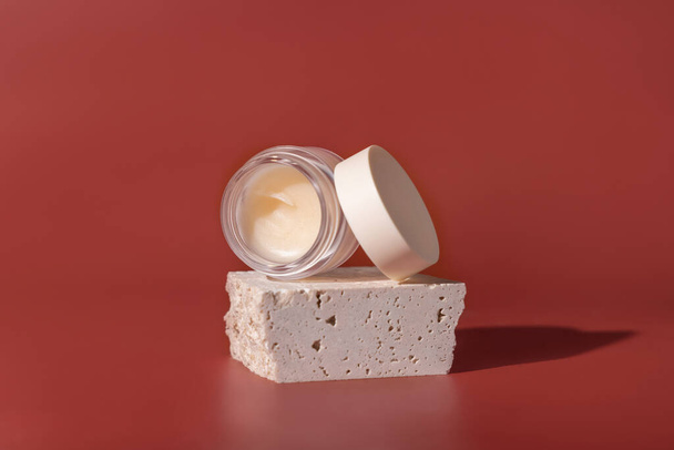 Smass Glass Cosmetic jar on travertine stones on red close up. Skincare beauty product package. Exotic natural cosmetics, pastel minimal compositio - Valokuva, kuva