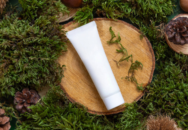 White plastic cream tube on wooden piece between green moss, pine cones and nuts, top view, mockup. Skincare beauty product package. Natural Organic Cosmetic concept.  - Foto, afbeelding