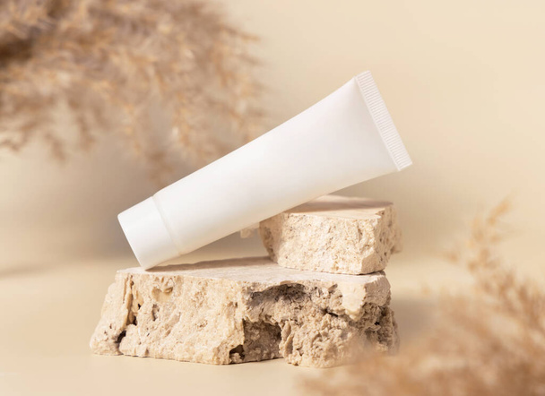 White plastic cream tube on travertine stone near dry pampas grass on light beige,  close up, mockup. Skincare beauty product. Natural cosmetics. Boho compositio - Valokuva, kuva
