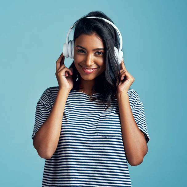 Nothing brings back good memories like music. a beautiful young woman wearing headphones against a blue background - Foto, Bild