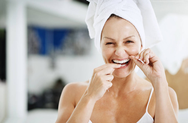 Flossing makes for healthy teeth. a mature woman flossing her teeth - Fotoğraf, Görsel