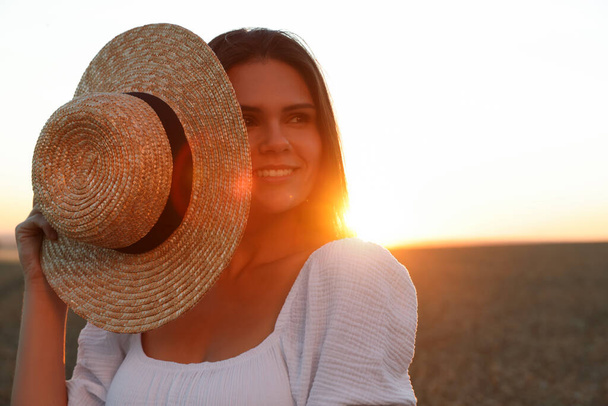 Beautiful young woman with straw hat in ripe wheat field at sunset, space for text - Photo, Image