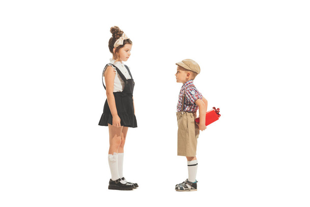 Gifts. Portrait of little boy and girl, charming kids in retro style outfit, american fashion of 60s, 70s years isolated on white background. Art, childhood, care. Copy space for ad. - Foto, Imagen
