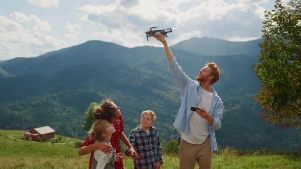 Happy family using drone on walk summer mountains. Red hair man launching quadcopter from hand outdoor. View of modern quadrocopter flying in cloudy sky operating by young guy. Technology concept. - 映像、動画