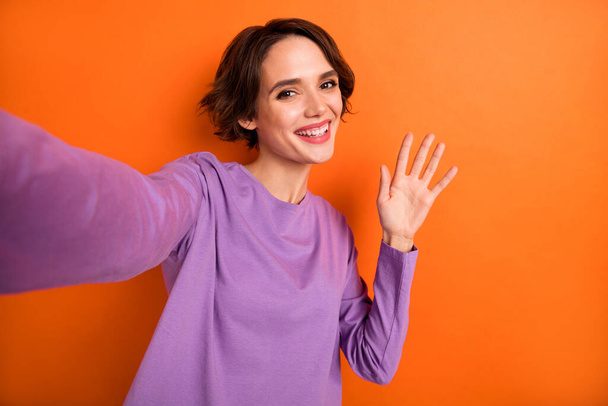 Portrait of pretty positive lady make selfie arm palm waving have good mood isolated on orange color background. - 写真・画像