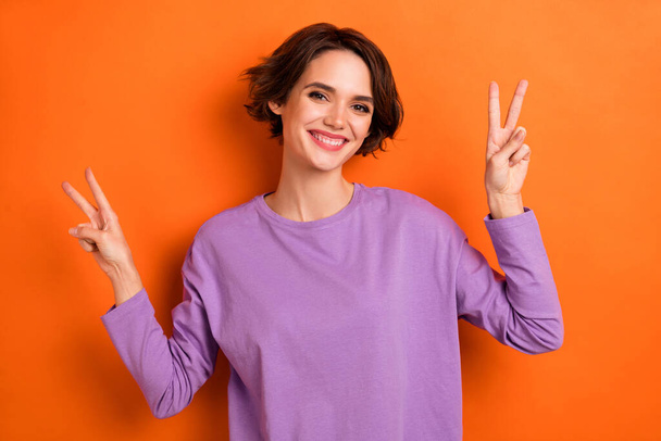 Photo of cheerful funny girl dressed purple pullover showing two v-signs isolated orange color background. - Fotografie, Obrázek