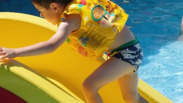 A 5-year-old boy in an inflatable life jacket rides down a slide in an aqua park. - Filmmaterial, Video