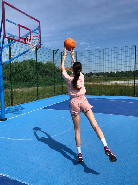 Young slim woman plays with a basketball and hits the hoop. - Photo, Image