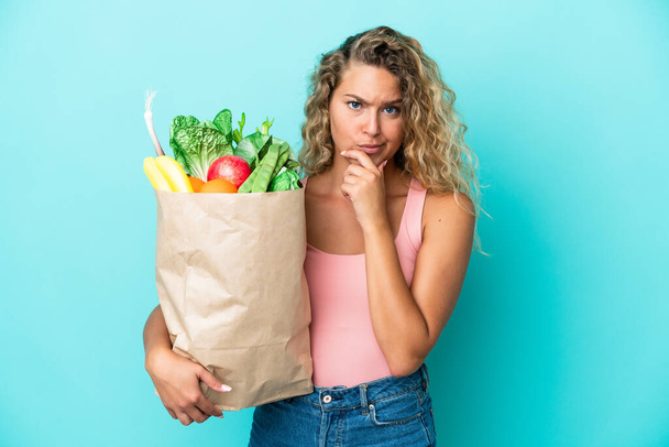 Girl with curly hair holding a grocery shopping bag isolated on green background thinking - Foto, afbeelding