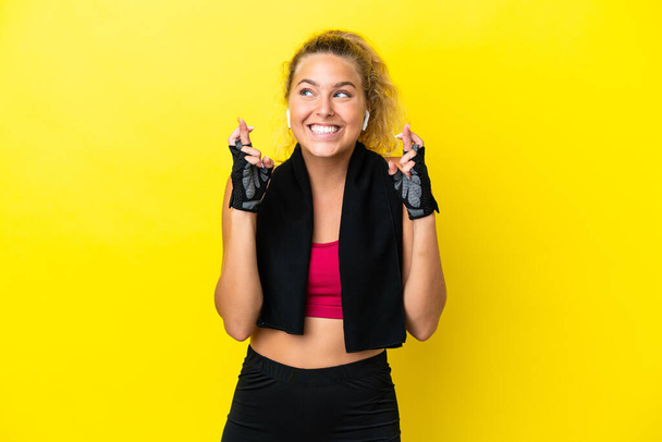 Sport woman with towel isolated on yellow background with fingers crossing - Foto, afbeelding