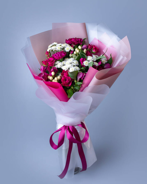 Bouquet of pink and white flowers wrapped in floral paper on a blue background. Original bouquet of pink roses, eustoma and white little asters. Concept of Womens Day, Mothers Day and Birthday. - Valokuva, kuva