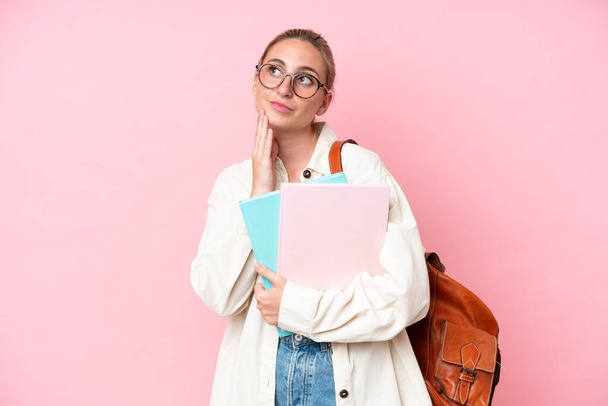 Young student caucasian woman isolated on pink background looking up while smiling - 写真・画像