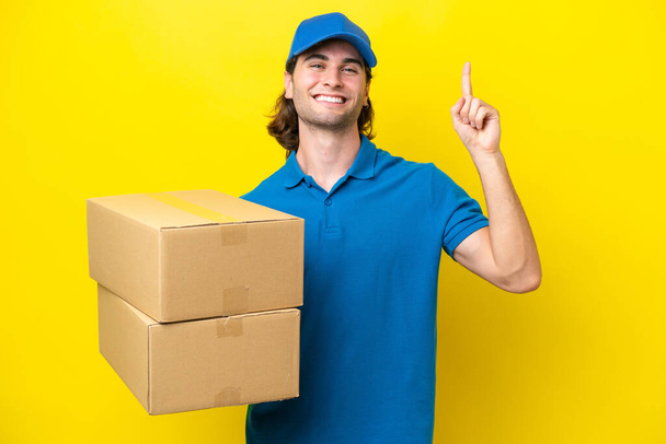 Delivery handsome man isolated on yellow background pointing up a great idea - Photo, image