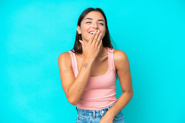 Young caucasian woman isolated on blue background happy and smiling covering mouth with hand - Foto, Imagem