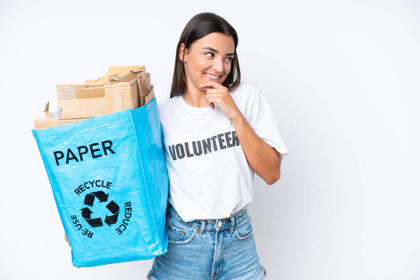 Young caucasian woman holding a recycling bag full of paper to recycle isolated on white background thinking an idea and looking side - Foto, Imagem