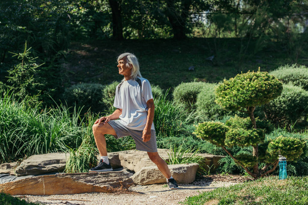 full length of cheerful senior man with grey hair exercising in sportswear outside - Foto, Imagen