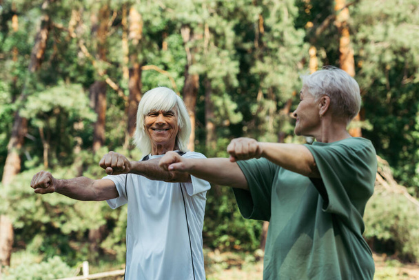 радостная пожилая пара в спортивной одежде, тренирующаяся с протянутыми руками в парке - Фото, изображение