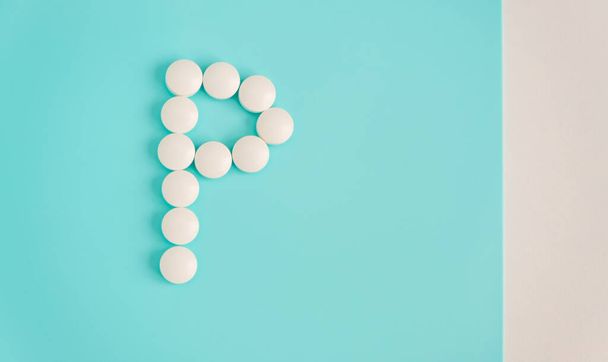 Letter P made from white pills on a blue background. White medical pills. Macro top view with copy space. Health care and pills concept, pharmaceutical, disease prevention - 写真・画像