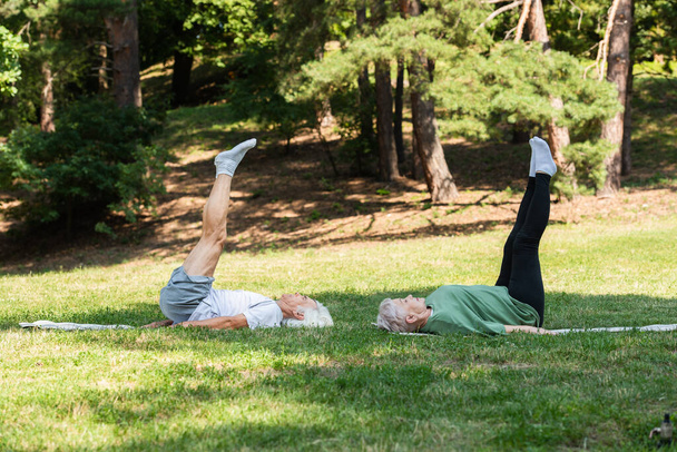 full length of senior couple in sportswear doing shoulder stand on fitness mats in green park  - Valokuva, kuva