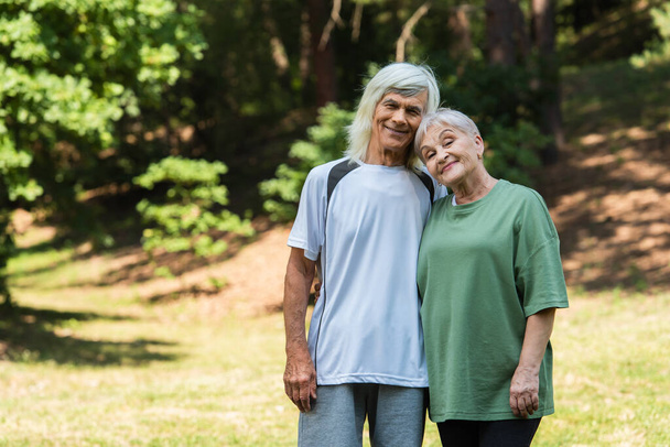 cheerful senior couple in sportswear hugging in green park  - Fotografie, Obrázek