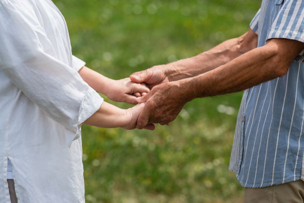 cropped view of senior husband and wife holding hands in summer - Foto, Imagen