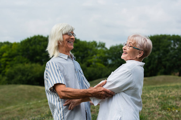 happy senior couple with grey hair looking at each other and smiling outside - Fotó, kép