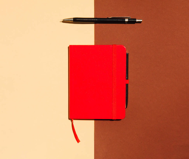 Top view of red notebook and pen on brown and beige background. Business or school concept. Flat lay, copy space. - Fotó, kép