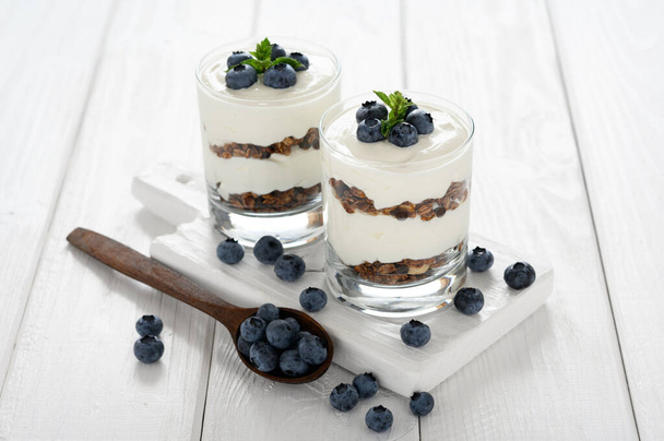 Dessert with cottage cheese, fresh blueberries and granola in a glass on a white wooden background. - Foto, Imagen