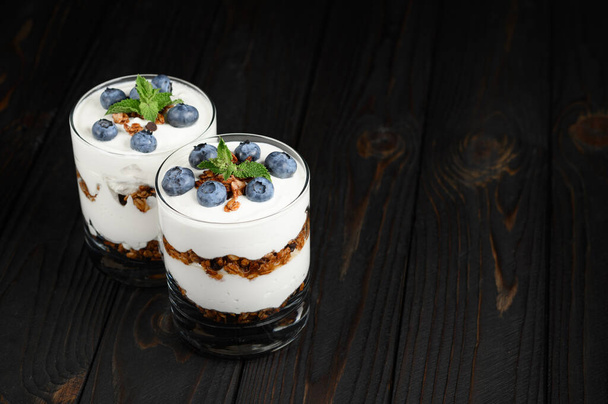 Homemade layered dessert with fresh blueberries, cream cheese or yogurt, granola on rustic background. - 写真・画像