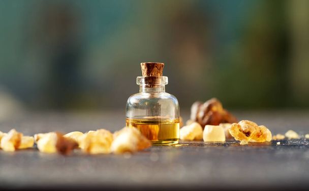 Стеклянная бутылка ароматерапевтического эфирного масла со смолой ладана на открытом столе - Фото, изображение