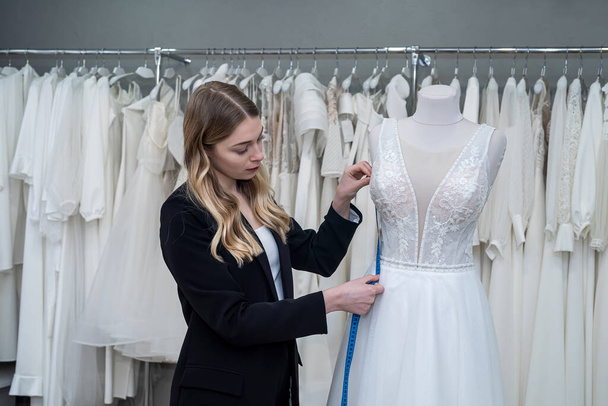 jolie femme tailleur utilisation ruban à mesurer pour les mesures robe de mariée sur mannequin en magasin  - Photo, image