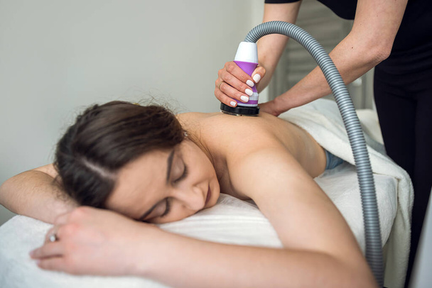 Young woman receives anti-cellulite massage on back with a hardware vacuum device in the spa. RF lifting procedure - Foto, Imagem