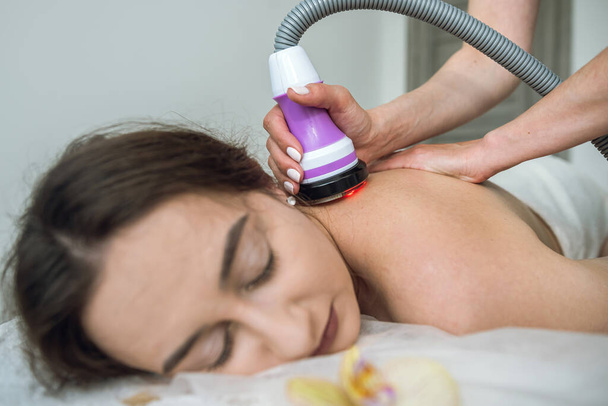 Young woman receives anti-cellulite massage on back with a hardware vacuum device in the spa. RF lifting procedure - Foto, Bild