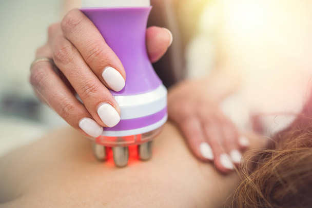 Молодая женщина получает антицеллюлитный массаж спины аппаратным вакуумным устройством в спа-салоне. RF-подъемник - Фото, изображение