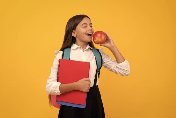 Az oktatás gyümölcse édes. A gyerek almát eszik, miközben tankönyveket tart. Élelmiszer oktatás. Iskolai nasi. Gyerekkori táplálkozás. Vissza a suliba. Tudásnap. - Fotó, kép