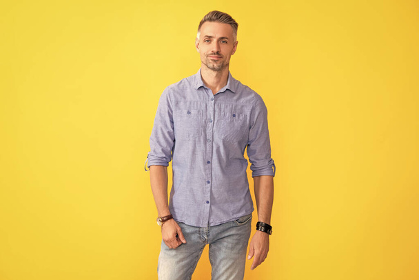 glimlachende volwassen man met handhorloge op gele achtergrond, mode-accessoire. - Foto, afbeelding