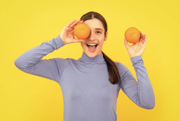 amazed young woman holding orange citrus fruit on yellow background, health. - Photo, image