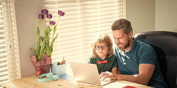 счастливый папа помогает своему школьному сыну ребенок в очках учиться с компьютером на дому, отцовство. - Фото, изображение
