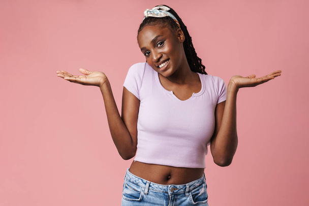 Black young woman with pigtails smiling and holding copyspace isolated over pink wall - Photo, image