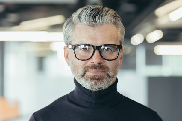 Close up photo portrait of successful senior and experienced businessman, man in glasses looking at camera, serious investor banker working in office at work - Fotografie, Obrázek