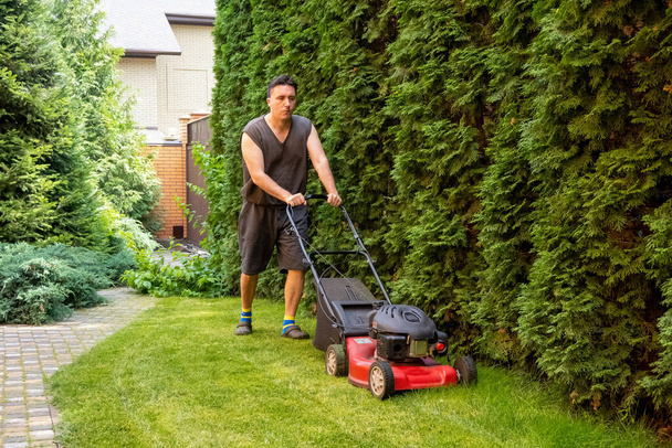 handsome man is cutting the lawn, process to cut the grass at the yard with special machine lawn mover, green garden - Fotó, kép