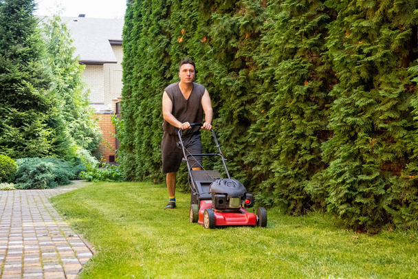 handsome man is cutting the lawn, process to cut the grass at the yard with special machine lawn mover, green garden - Fotoğraf, Görsel