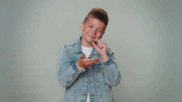 Need some more please give me. Boy showing a little bit gesture with sceptic smile, showing minimum sign, measuring small size, asking for help. Children teenager child kid on gray studio background - Materiał filmowy, wideo