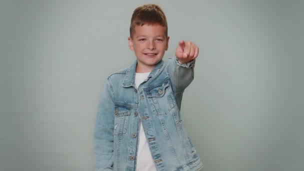 Call me, here is contact number. Toddler boy in jeans jacket looking at camera doing phone gesture like says hey you call me back. Young teenager schoolboy child kid isolated on gray wall background - Filmati, video