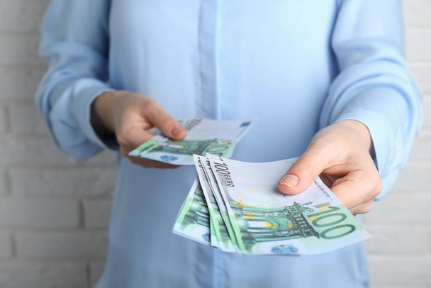 Woman holding 100 Euro banknotes near white brick wall, closeup. Money exchange - Fotografie, Obrázek