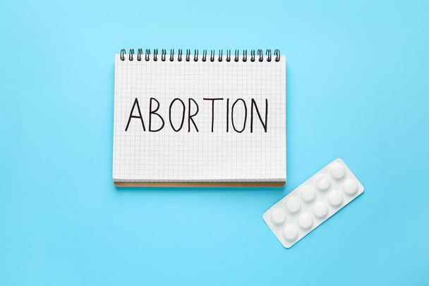Notebook with word Abortion and pills on light blue background, flat lay - Foto, Imagem