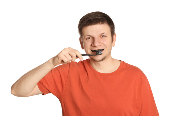 Man brushing teeth with charcoal toothpaste on white background - Foto, afbeelding