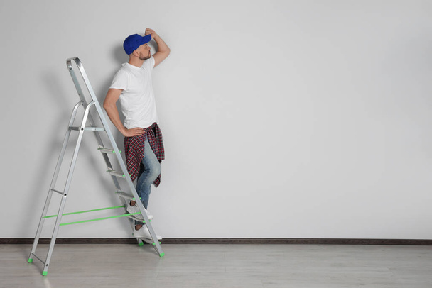 Handsome man on ladder near white wall indoors, space for text - Foto, Imagen