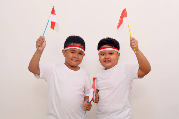 Two asian boys holding Indonesian flag to celebrate independence day. Isolated on white background - Foto, afbeelding